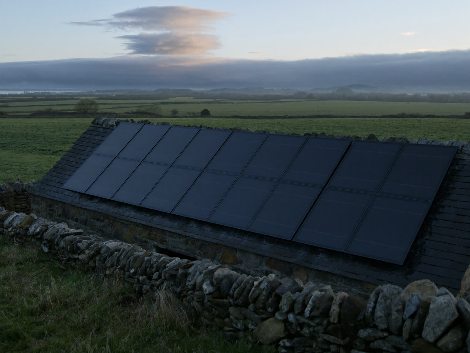 Matte black solar panels on a stone barn roof in the Eden Valley at dawn